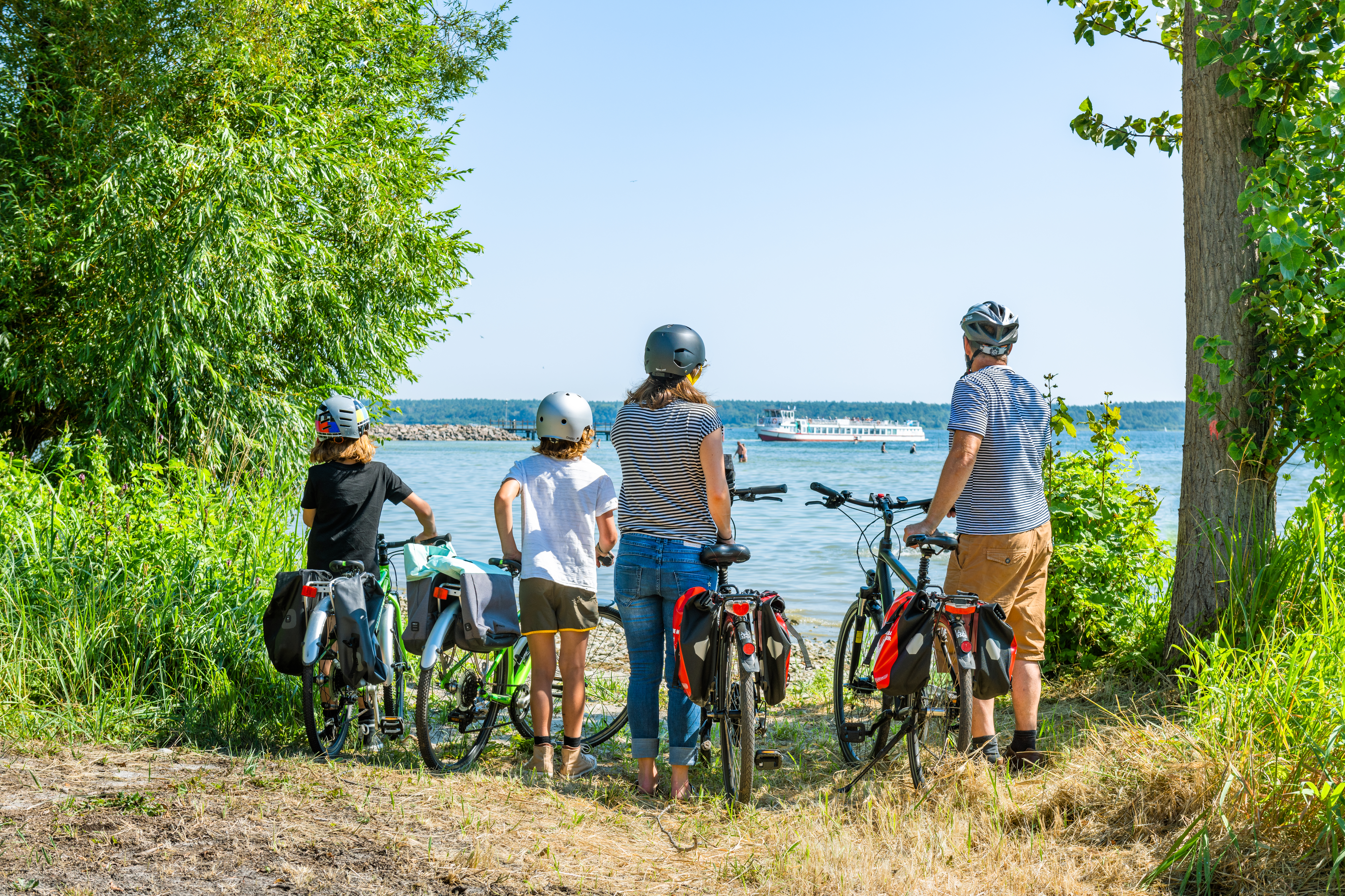 Eine Familie mit Eltern und zwei Kindern steht mit ihren Fahrrädern am Ufer der Müritz und blickt aufs Wasser